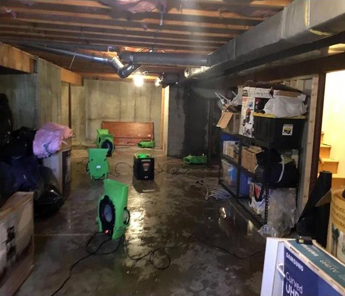 A wet basement with wet concrete floors and wet ceiling and insulation above.  Air movers and dehumidifiers are visible.