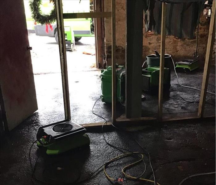Basement room with a wet, dirty floor and SERVPRO drying equipment