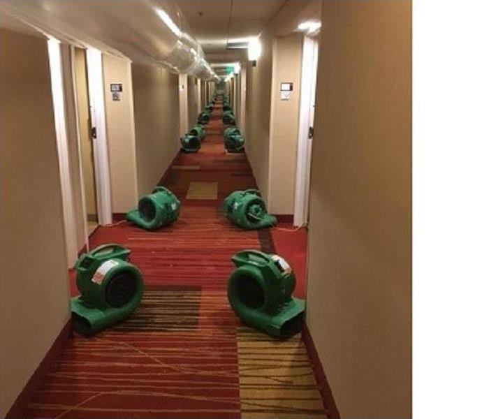 Water damaged long hotel hallway with air movers positioned on both sides in front of each room dooway