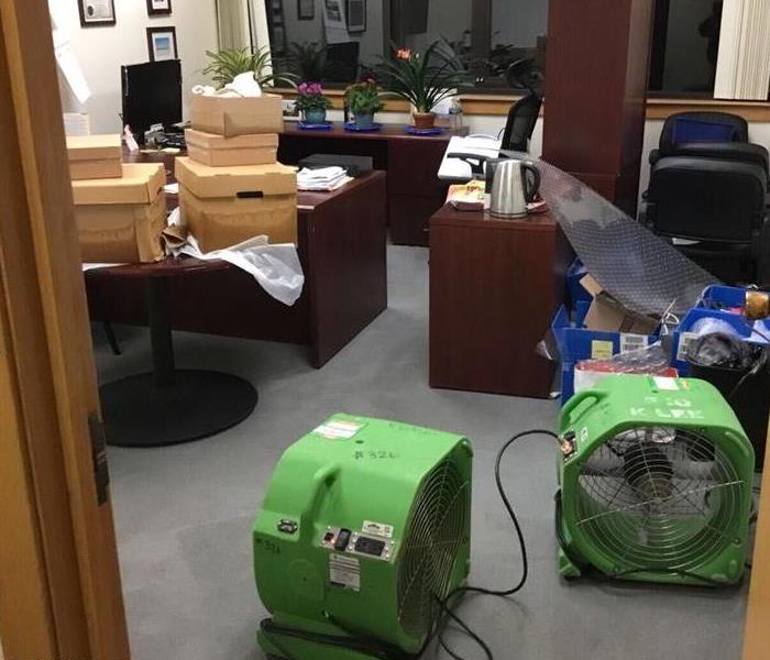 Air movers circulating dehumidified air around an office affected by water damage, with it's contents boxed and stacked