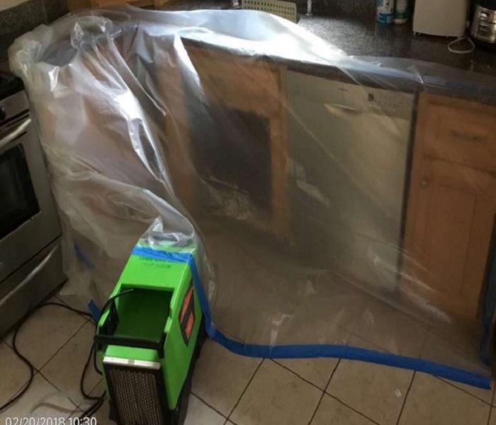 A kitchen cabinets and a dehumidifier covered in plastic to limit the air space of the area to be dried