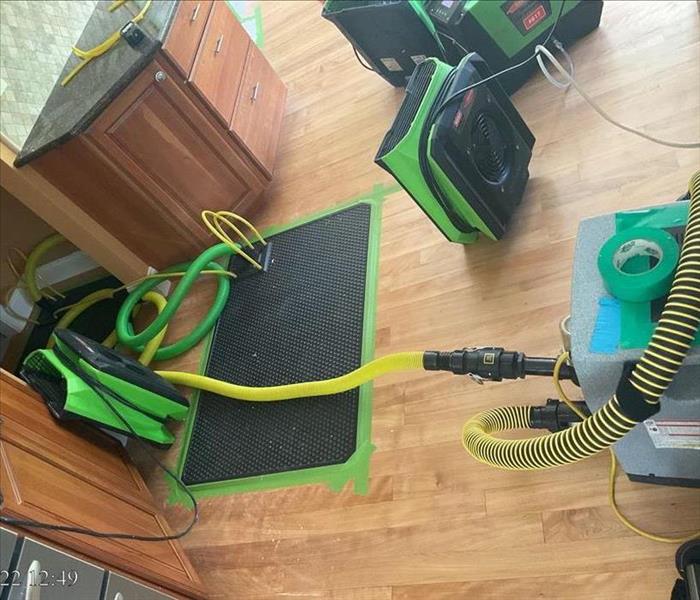 A rubber extraction mat sealed on a wood floor, two air movers, and a dehumidifier drying a wood kitchen floor